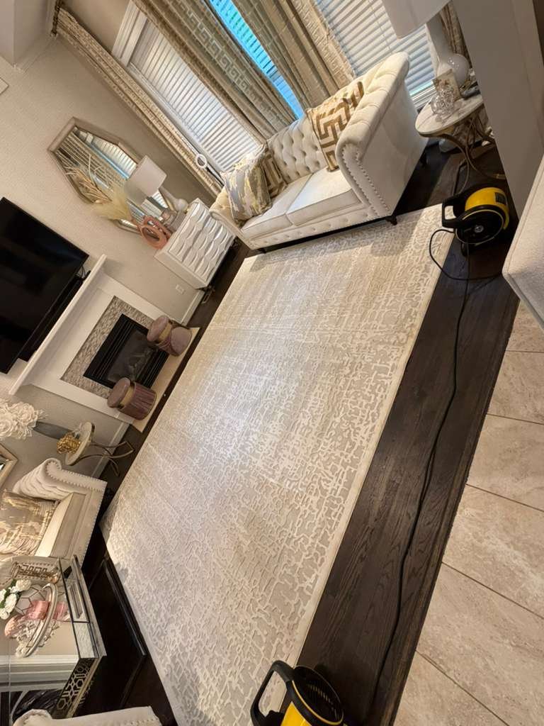 A cream area rug on hardwood flooring drying under a yellow air mover beside a fireplace